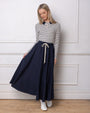Model wearing navy maxi skirt and striped polo standing against a white wall.