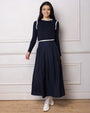 Model wearing a navy pleated skirt and navy top standing against a white wall.