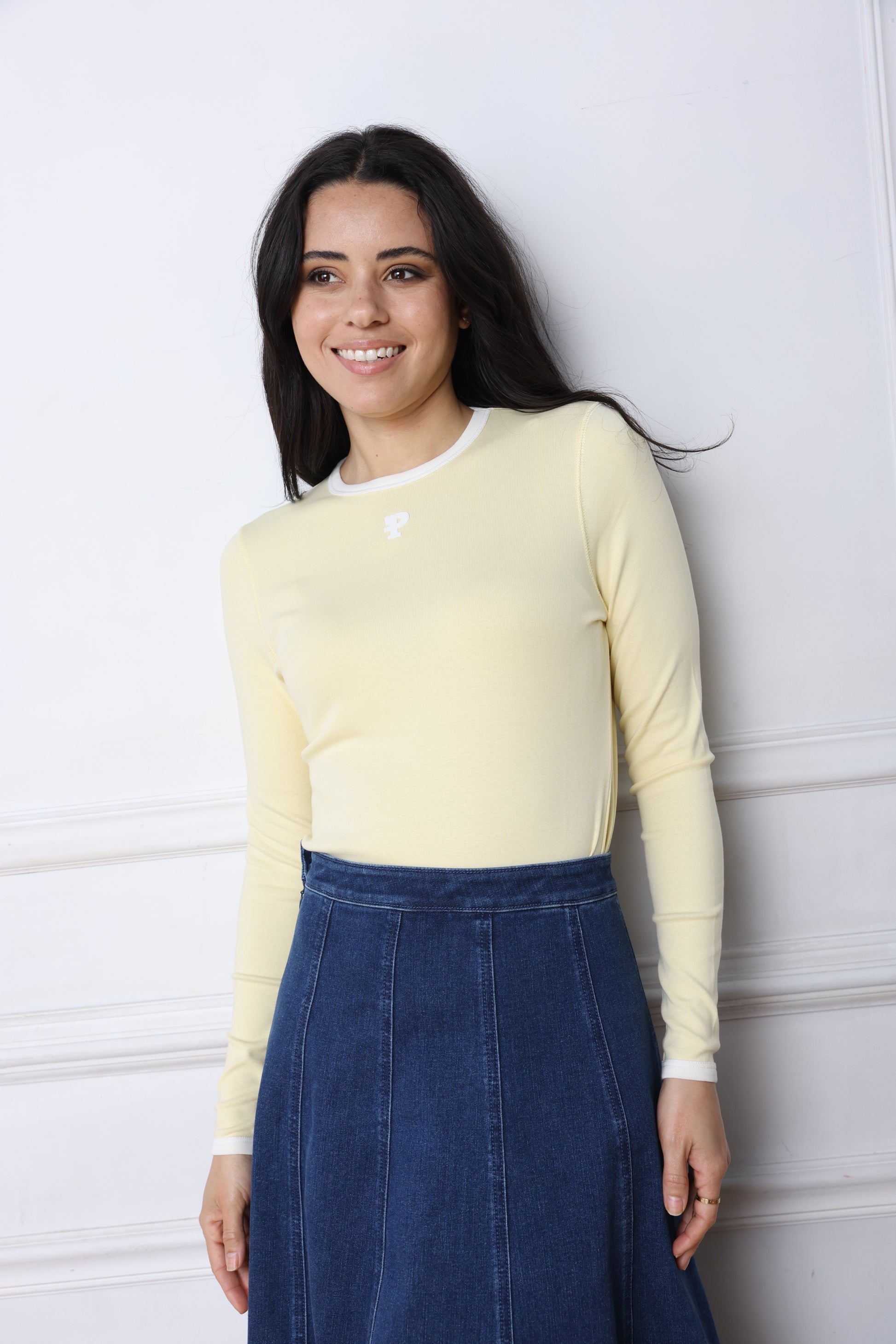 Woman wearing a yellow top and blue jeans lying on a white floor.