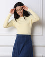 Woman wearing a light yellow sweater and blue skirt against a white wall