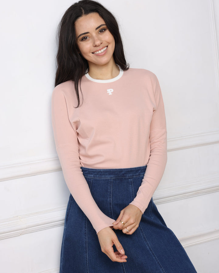 Woman wearing a pink sweatshirt with a logo on a white floor