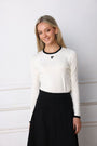Woman wearing a white long-sleeve top with a black logo and a black skirt against a white background