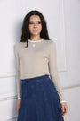Woman wearing a beige long-sleeve top and blue skirt against a white wall
