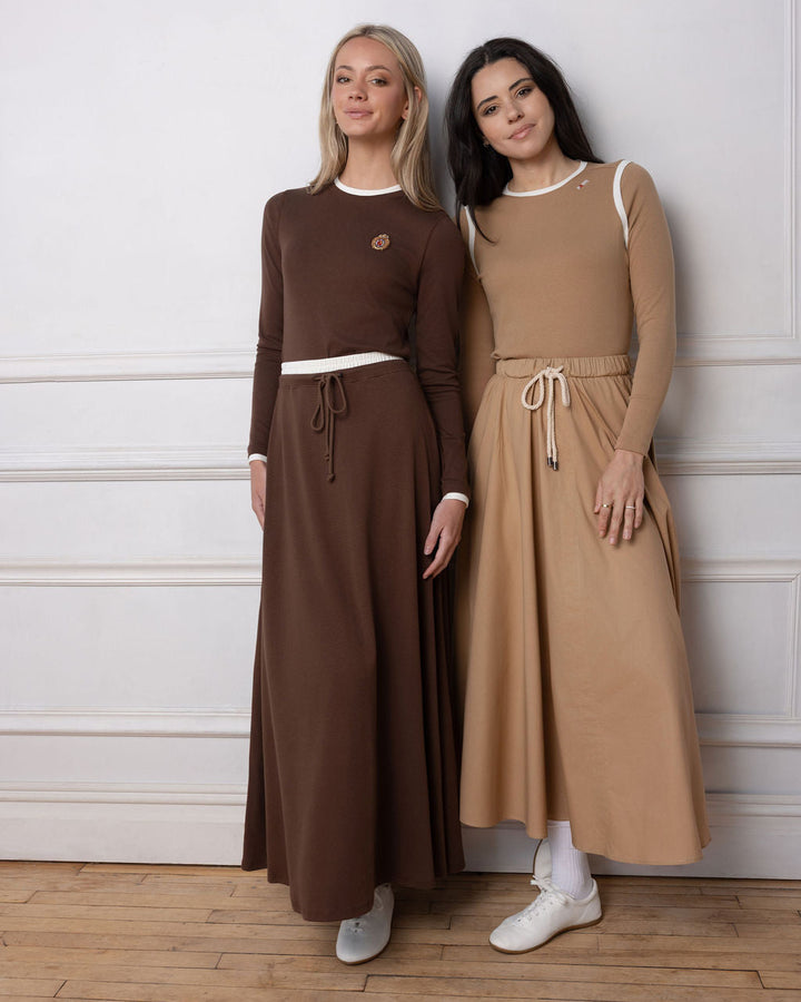 two models wearing maxi skirts and matching tops standing against a white wall.