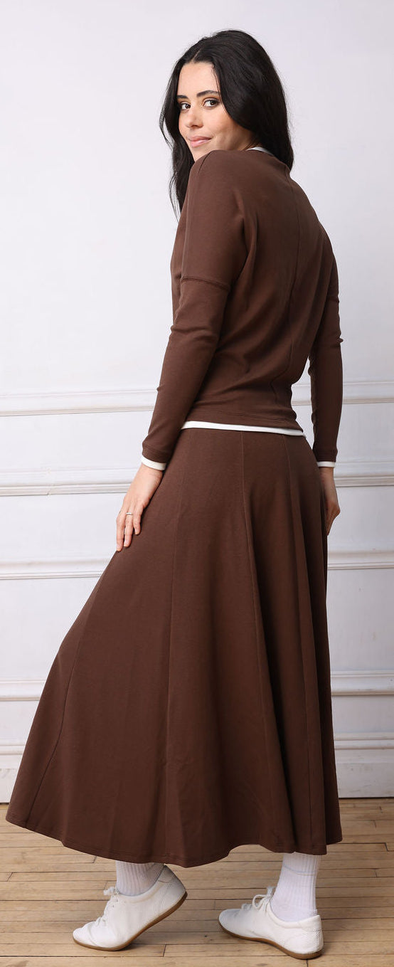 Woman wearing a brown dress standing against a white wall.