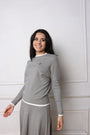 Woman wearing a gray sweater and skirt against a white wall