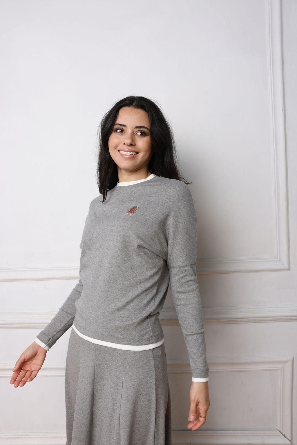 Woman wearing a gray sweater and skirt against a white wall