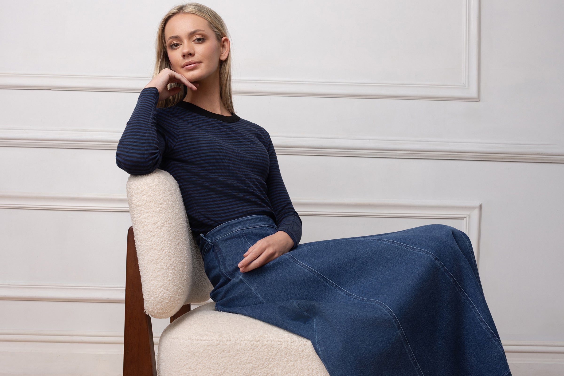 Woman sitting on a chair wearing a blue outfit against a white wall.