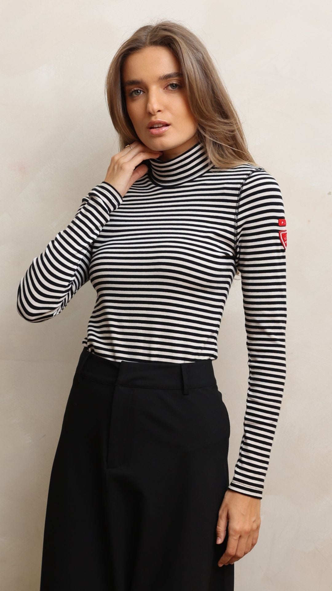 Woman wearing a black and white striped turtleneck with a visible brand logo against a neutral background