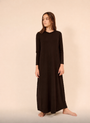 A woman modeling a long-sleeved, ankle-length dark brown nightgown  against a solid beige studio background.