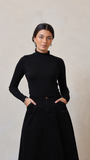 Woman wearing a black turtleneck and black skirt against a plain background