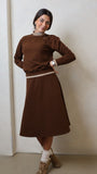 Woman wearing a brown sweater and skirt set against a plain background