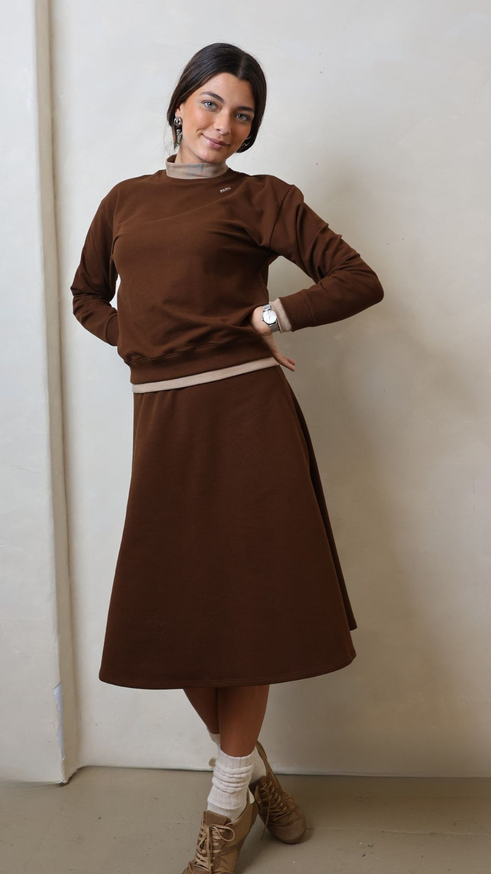Woman wearing a brown sweater and skirt set against a plain background