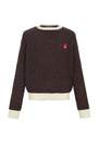 A dark brown ribbed knit sweater with cream-colored ribbed trim at the crew neck, hem, and cuffs, featuring a small red embroidered logo on the left chest.