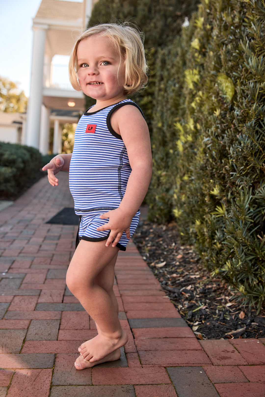 Child wearing a striped swimsuit standing on a brick path outdoors.