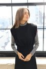 Woman in a black blazer with striped sleeves standing in front of large windows.
