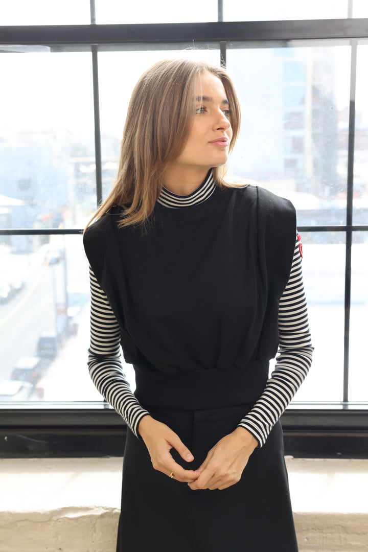 Woman in a black blazer with striped sleeves standing in front of large windows.