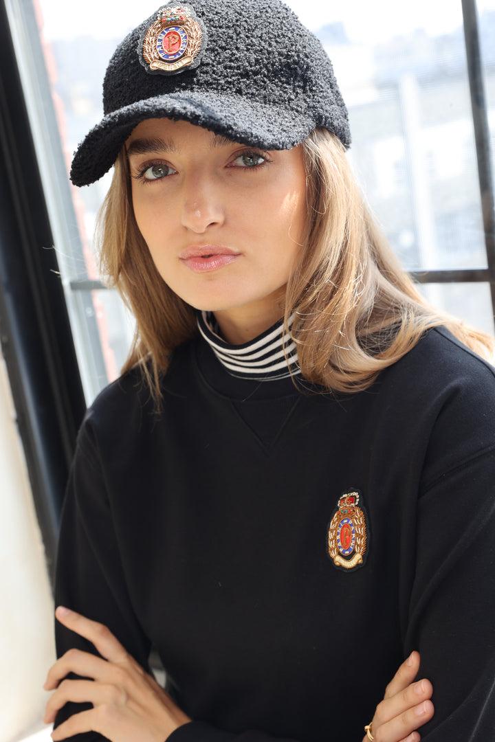 Person wearing a black outfit with embroidered logos and a gray knit hat.