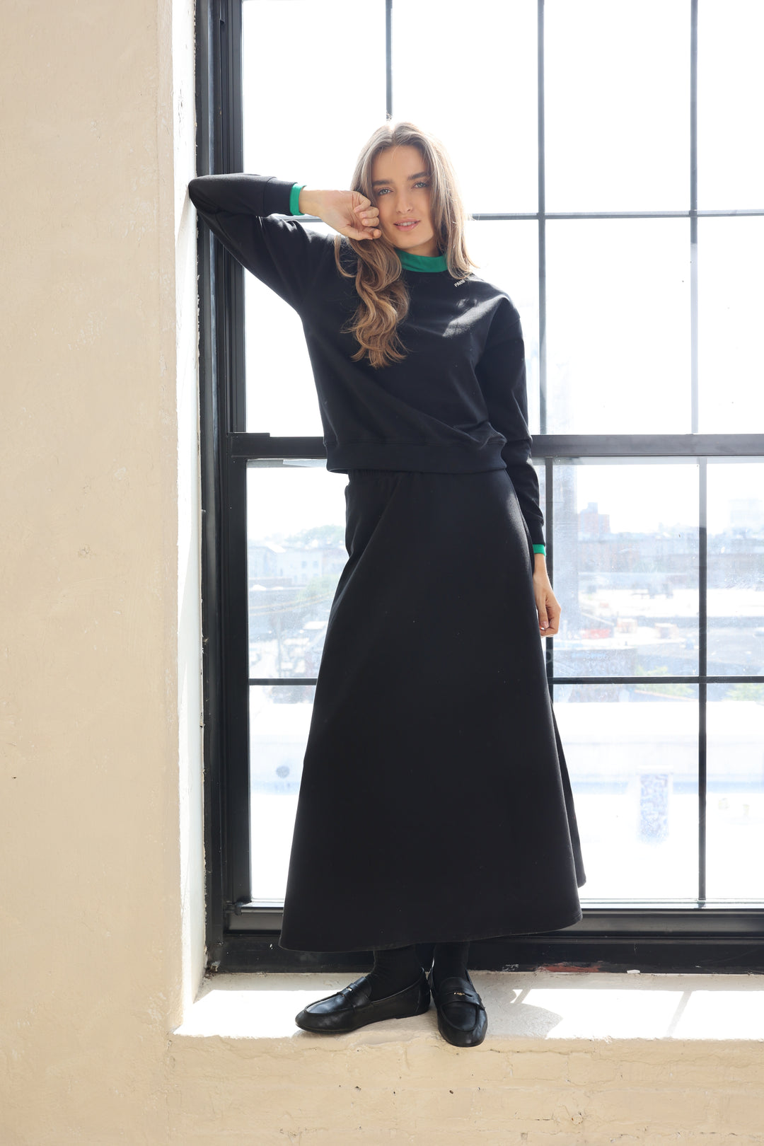 Person wearing a black skirt standing in front of a large window.