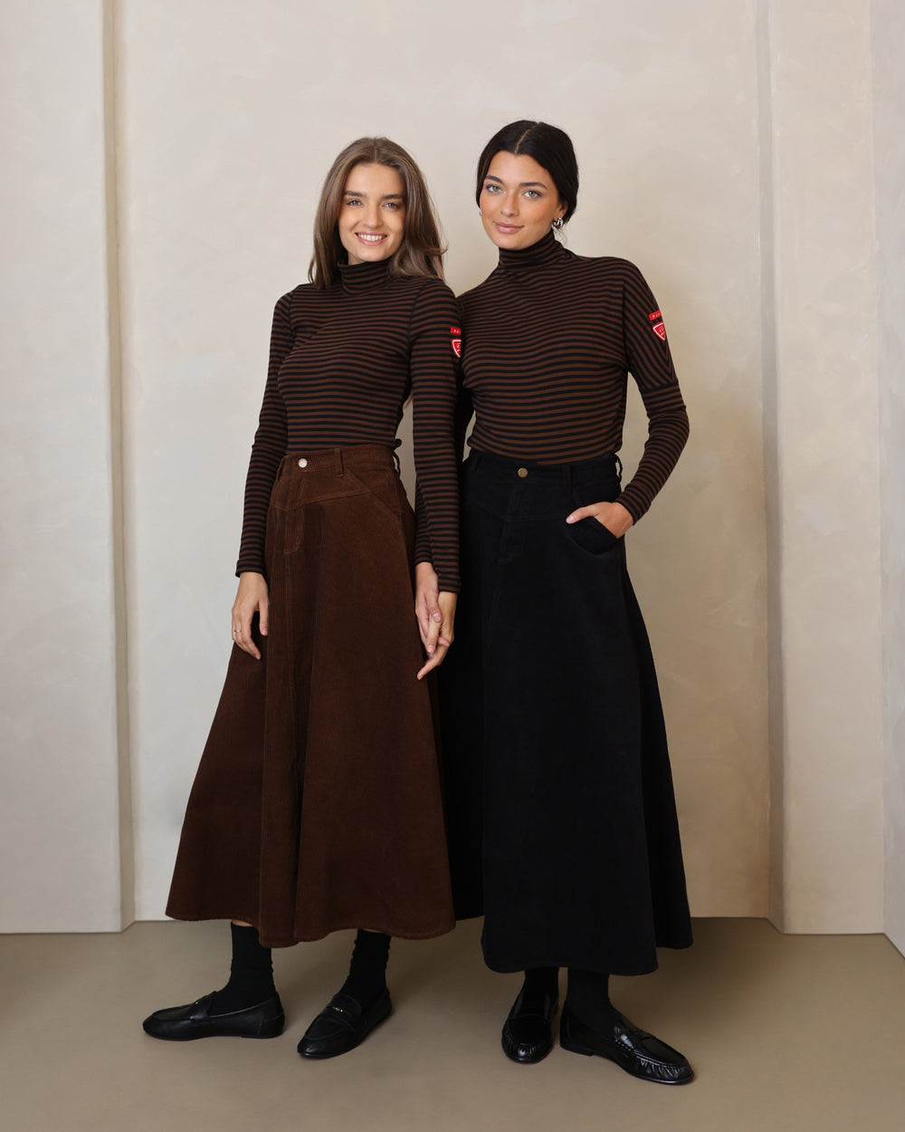 Two women wearing matching brown outfits standing in front of an archway.