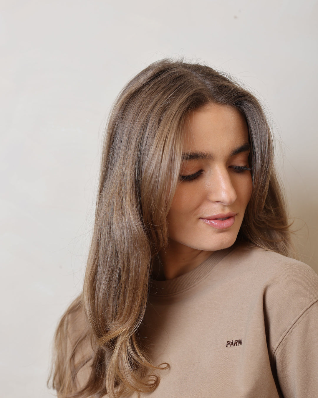Woman with long hair wearing a beige sweatshirt on a plain background