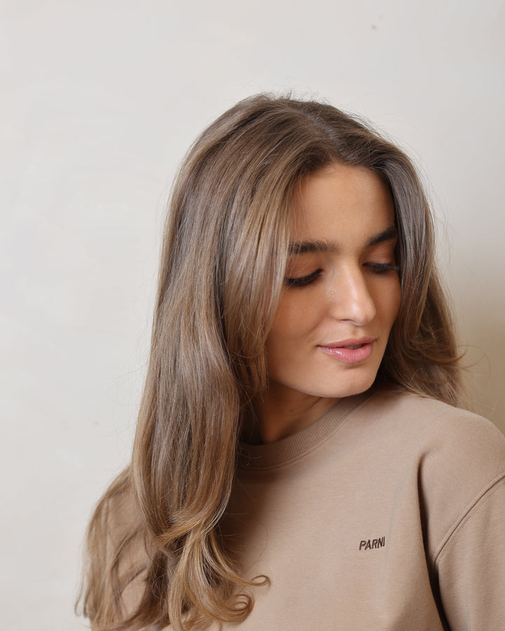Woman with long hair wearing a beige sweatshirt on a plain background