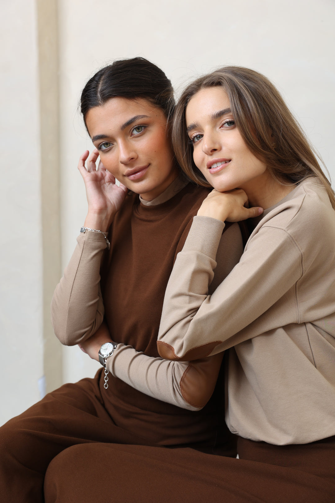 Two people lying on a white surface, wearing brown and beige clothing.