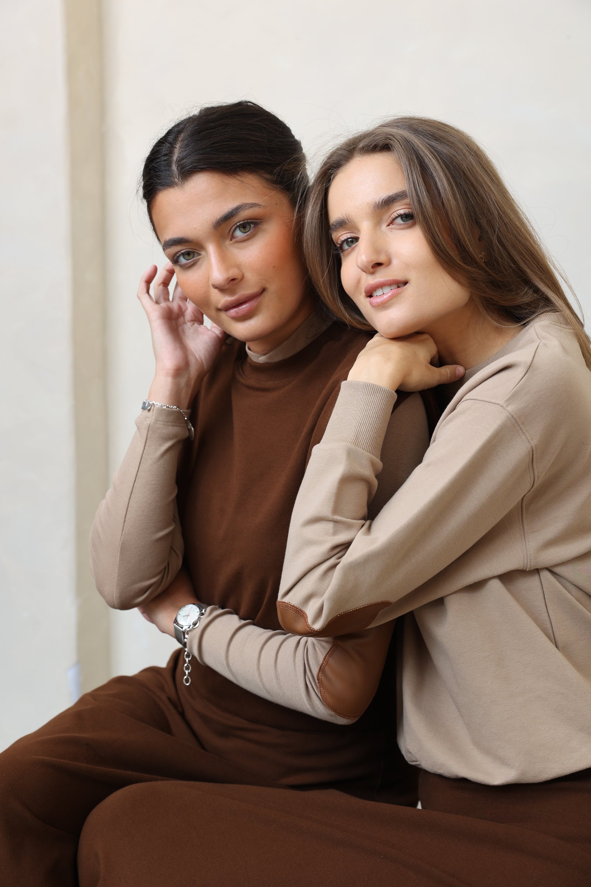 Two people lying on a white surface, wearing brown and beige clothing.