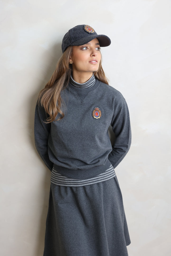 Person wearing a gray tracksuit with a logo and a matching cap on a light background