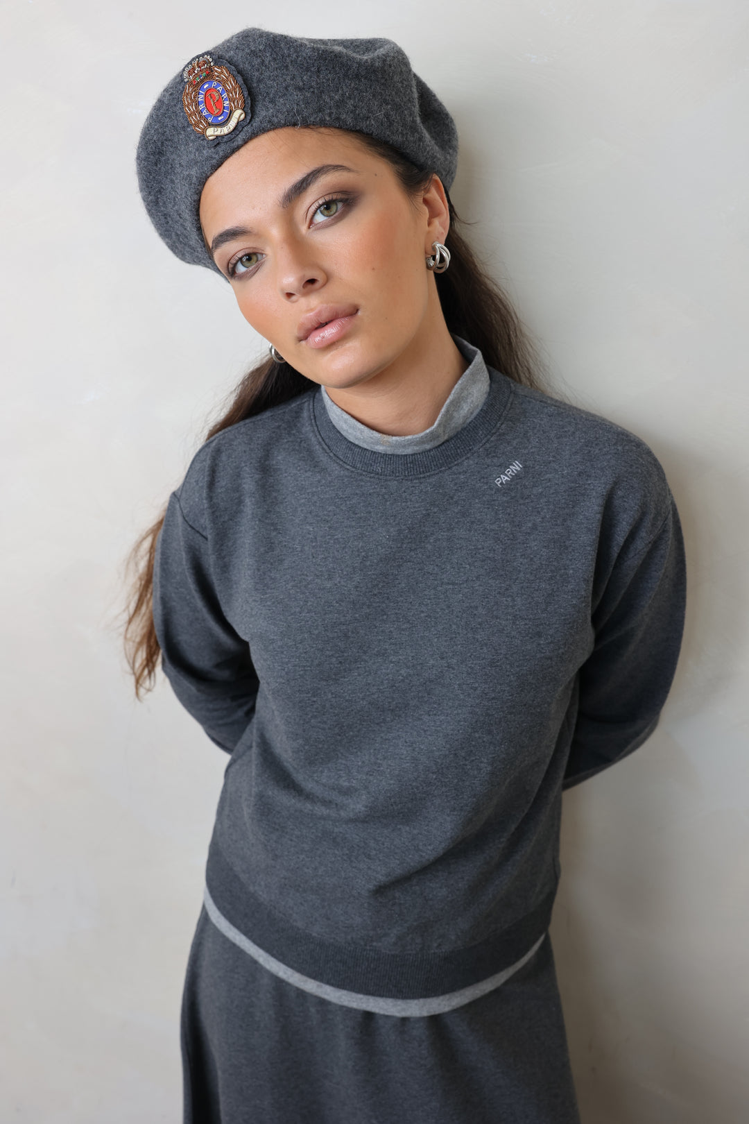 Person wearing a gray outfit and hat on a light background