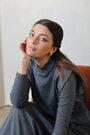 Woman in a gray dress sitting on a chair with a plain background