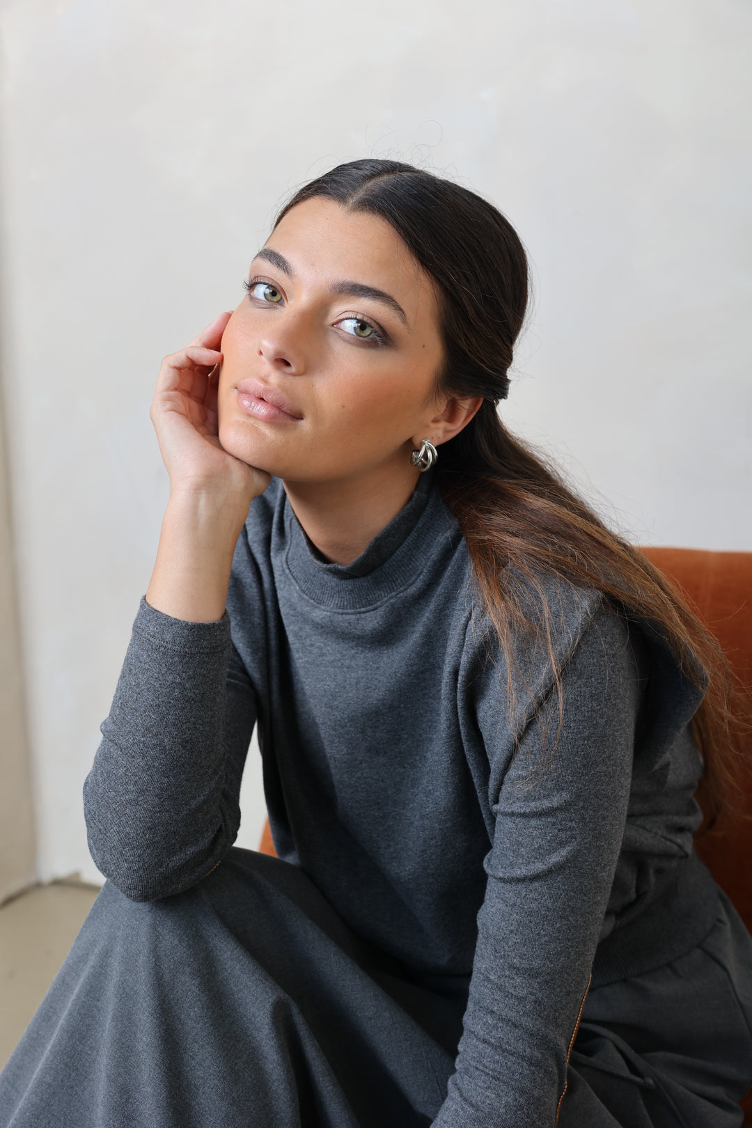 Woman in a gray dress sitting on a chair with a plain background