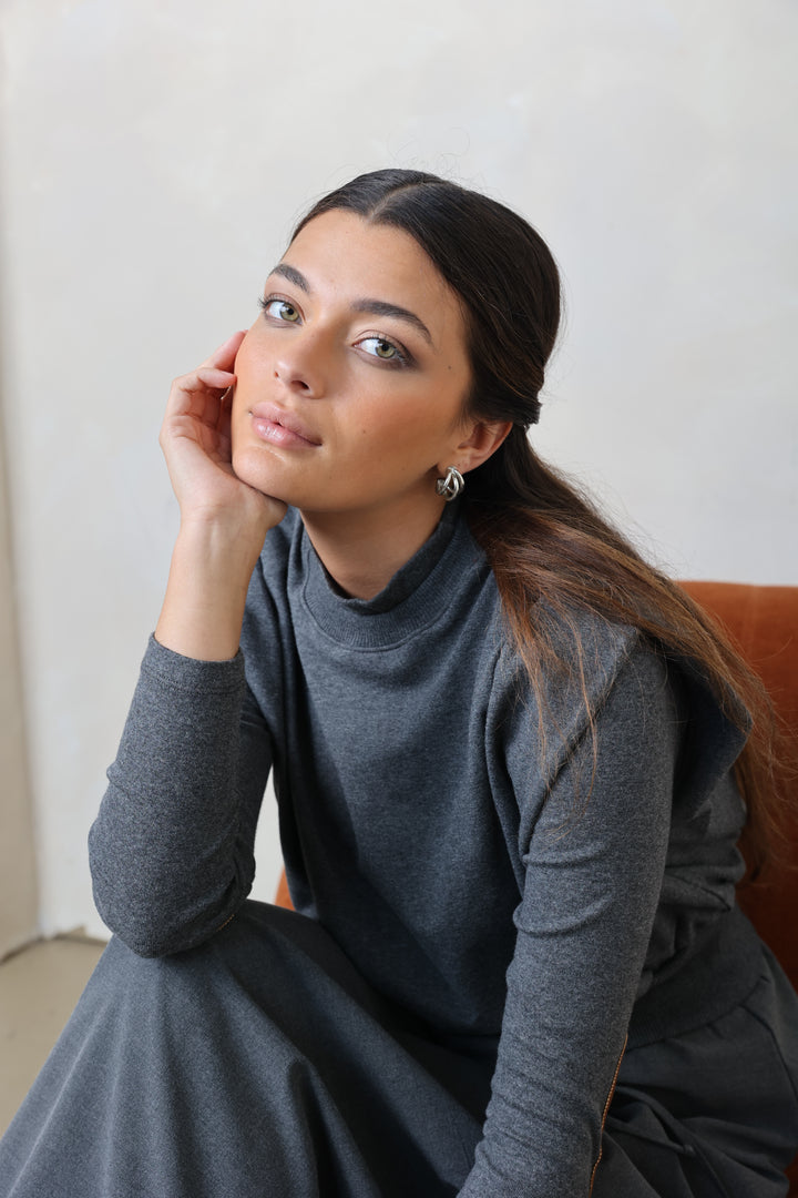 Woman in a gray dress sitting on a chair with a plain background