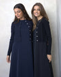 Two women wearing matching navy blue outfits with white buttons against a plain background