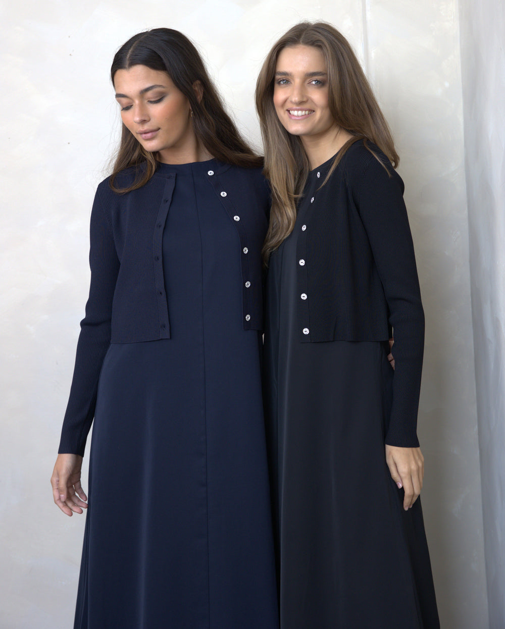Two women wearing matching navy blue outfits with white buttons against a plain background