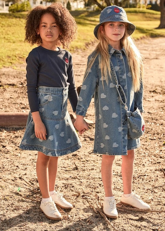 Two young girls wearing matching denim outfits with heart patterns outdoors.