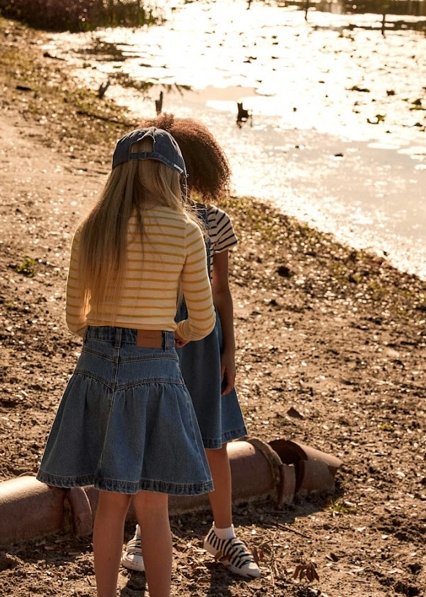 Two children standing by a body of water, looking at ducks.