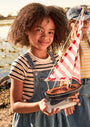 Child holding a model sailboat by a body of water with another person in the background.