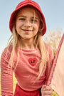 Young girl wearing a red hat and striped shirt with a heart design outdoors.