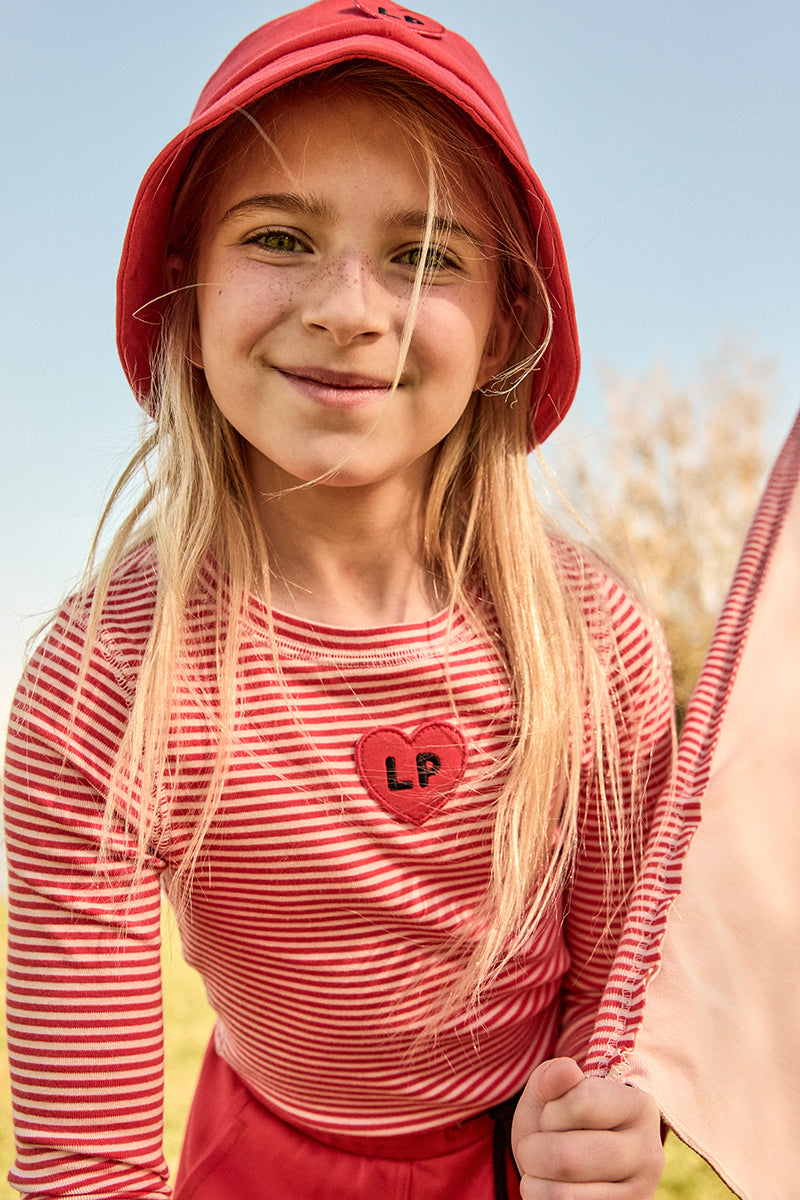 Young girl wearing a red hat and striped shirt with a heart design outdoors.