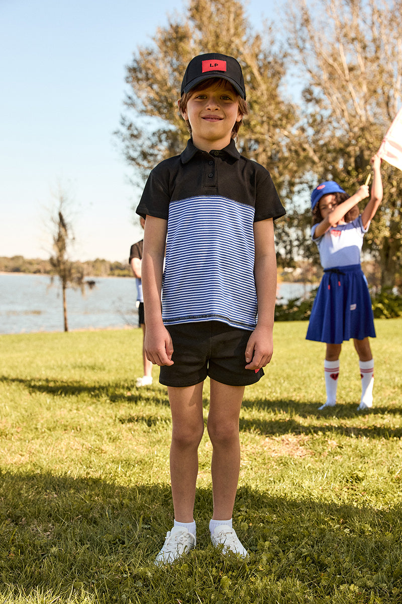 Child wearing a black and white striped polo shirt with a cap in an outdoor setting.