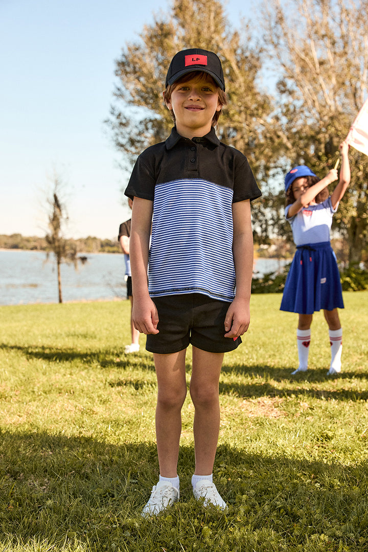 Child wearing a black and white striped polo shirt with a cap in an outdoor setting.