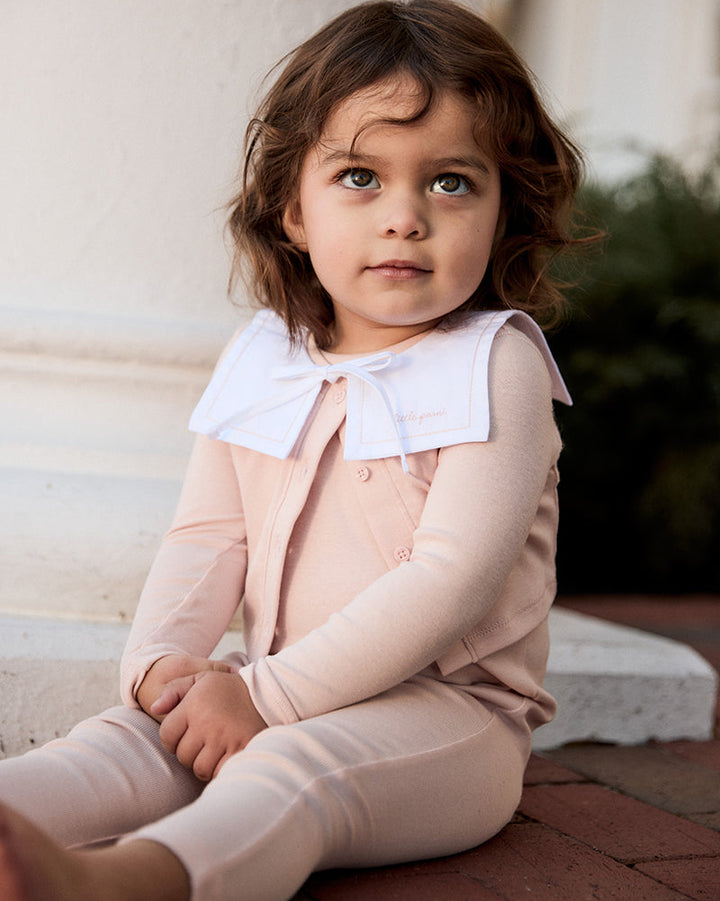 Young girl in a pink outfit sitting on a stone step outdoors.