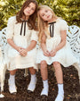Two young girls in matching white dresses with black ribbons sitting on a bench outdoors.