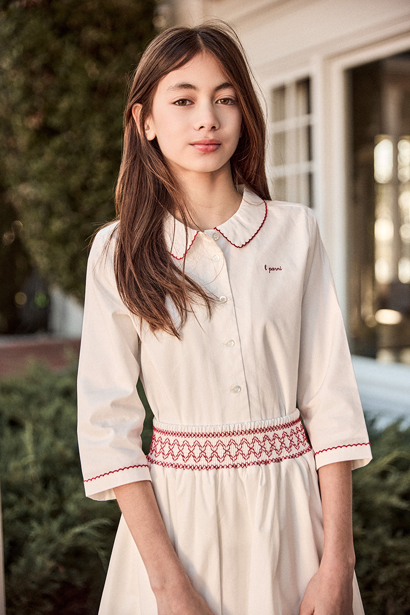 Woman wearing a cream-colored dress with red embroidery outdoors