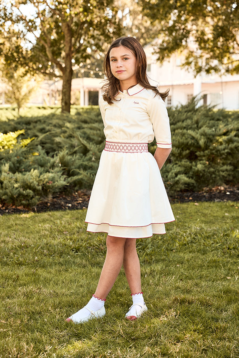 Young girl in a white dress standing on grass with trees in the background