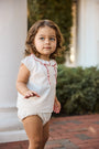 Child wearing a white outfit with red trim outdoors