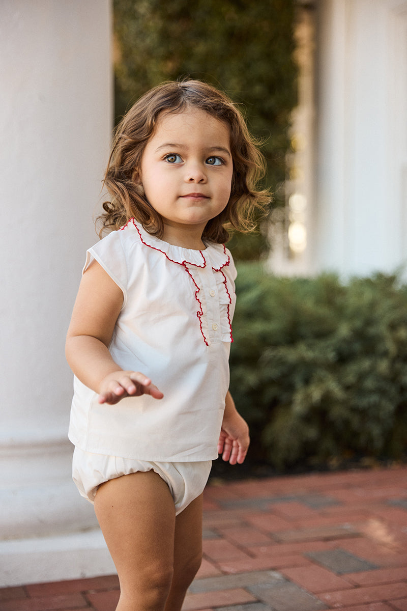 Child wearing a white outfit with red trim outdoors