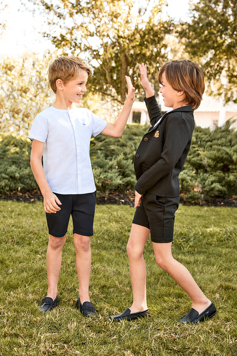 Two children giving each other a high-five outdoors on a grassy area with trees in the background.