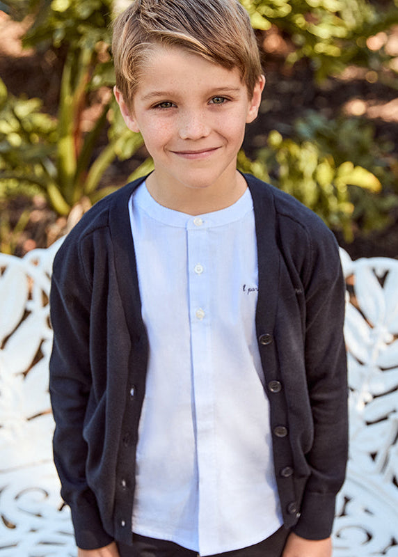 Young boy standing on a decorative white bench with greenery in the background